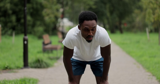 Retrato de homem cansado corredor preto respirando depois de correr no parque da cidade. Atleta afro-americano tem pausa após exercícios de corrida no parque de verão. Feche o homem esporte descansando após o treino ao ar livre.