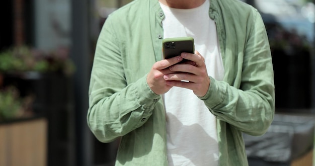 Retrato de homem casual usando smartphone ao ar livre Homem alegre digitando mensagens no telefone fora de mensagens on-line e navegando na internet