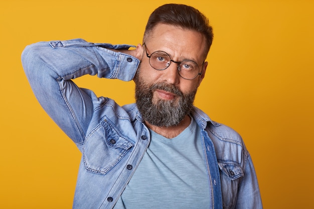 Retrato de homem caucasiano barbudo bonito com penteado elegante, segurando as mãos atrás da cabeça