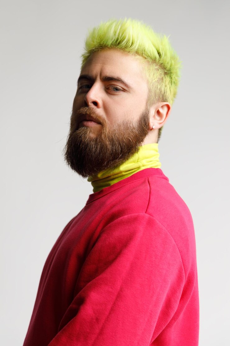 Foto retrato de homem caucasiano barbudo jovem bonito orgulhoso na camisola casual vermelha, olhando com cara de orgulho, de pé meio presunçoso para o lado inchado. tiro de estúdio interior isolado em fundo cinza.