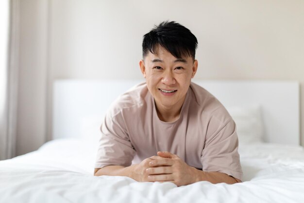 Retrato de homem chinês bonito feliz deitado na cama