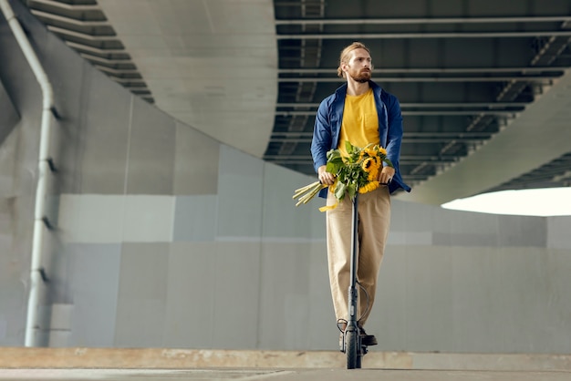 Foto retrato de homem com girassóis na scooter elétrica ao ar livre