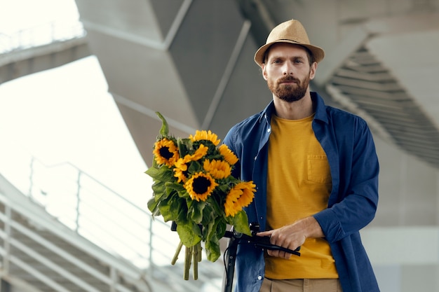 Foto retrato de homem com girassóis na scooter elétrica ao ar livre