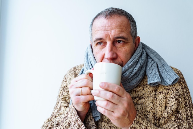 Retrato de homem com roupas quentes doente com uma xícara de chá quente em uma xícara