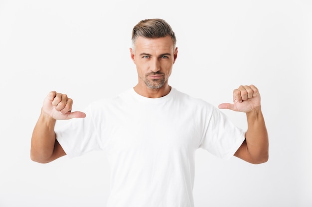 Retrato de homem confiante na casa dos 30 anos com cerdas vestindo uma camiseta casual apontando os dedos para si mesmo isolado no branco