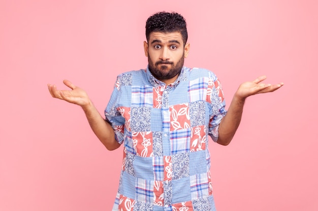 Retrato de homem confuso sem noção na camisa azul estilo casual encolhendo os ombros como não sabe a resposta, não pode tomar uma decisão, sendo incerto, não tenho certeza. Tiro de estúdio interior isolado no fundo rosa.