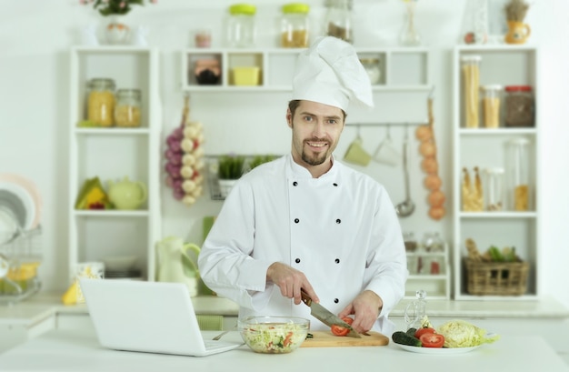 Retrato de homem cozinhando na cozinha com laptop