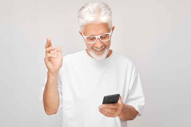 Retrato de homem de cabelos grisalhos de camisa branca segurando um telefone móvel na mão com rosto sorridente feliz Pessoa com smartphone isolado em fundo branco