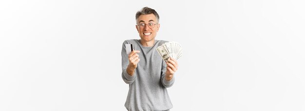Foto retrato de homem de meia-idade animado e feliz olhando espantado com o cartão de crédito e o dinheiro em pé sobre w