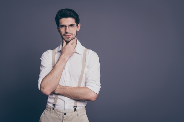 retrato de homem de negócios atraente aparência encantadora segurando o braço no queixo profundamente vestido formalwear camisa branca bege suspensórios especificações.