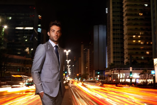 Retrato de homem de negócios e luzes da cidade à noite com tráfego como conselheiro financeiro para edifício profissional corporativo ou tarde Pessoa masculina rosto e terno com desfocamento de movimento na rua urbana ou deslocar-se