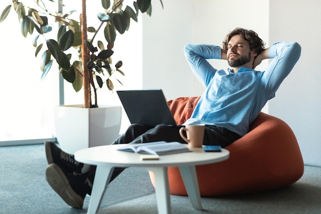 Retrato de homem de negócios sorridente relaxando no pufe no escritório