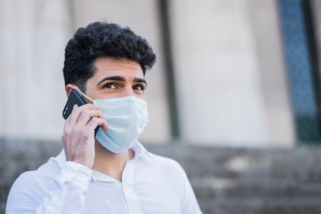 Retrato de homem de negócios usando máscara facial e falando ao telefone enquanto está sentado na escada ao ar livre