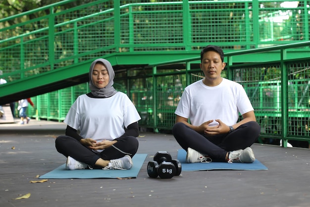 Retrato de homem e mulher muçulmana sentado na esteira e meditando em pose de lótus. Casal curtindo a paz