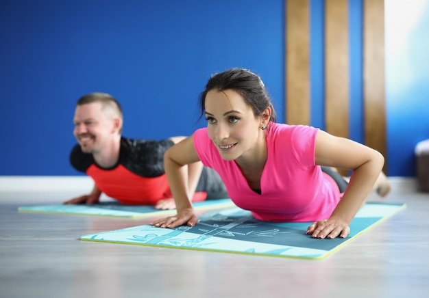 Retrato de homem e mulher sorridentes fazendo exercícios para o objetivo corporal adequado, trem ativo pela manhã. Roupas esportivas e tapetes no chão. Ioga, hobby, conceito de motivação