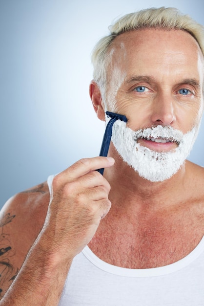 Retrato de homem e navalha com creme de barbear para cuidar da pele da barba ou depilação contra fundo de estúdio Rosto masculino maduro com creme de barbear ou produto de espuma para higiene ou tratamento facial