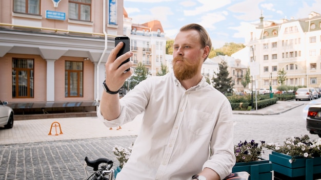 Retrato de homem elegante hippie barbudo usando smartphone na rua da cidade.