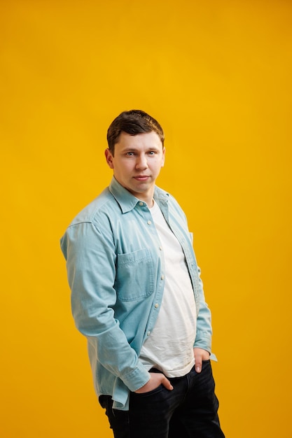 Retrato de homem europeu bonito na camisa olhando para a câmera em pé no fundo do estúdio amarelo