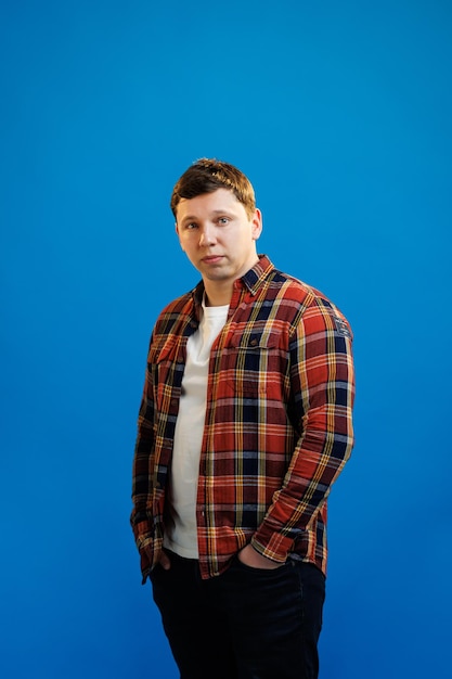 Retrato de homem europeu bonito na camisa olhando para a câmera em pé no fundo do estúdio azul