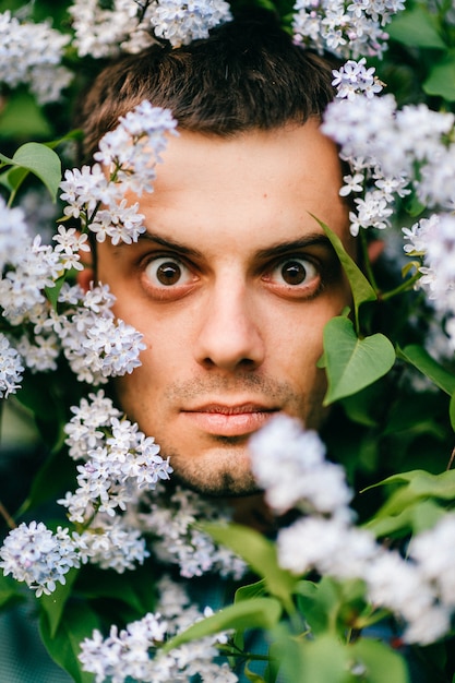 Retrato de homem expressivo através de arbustos lilás florescendo