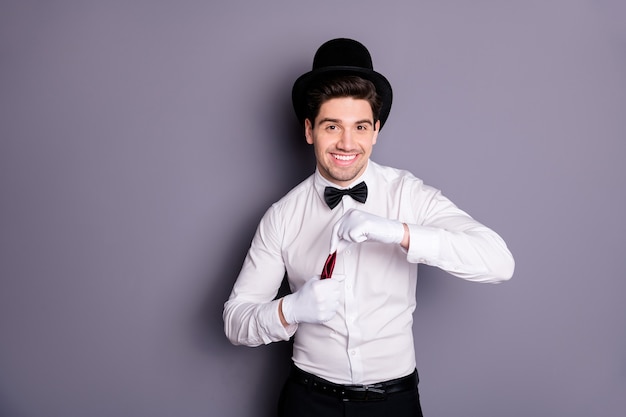 Retrato de homem feiticeiro alegre e positivo esconder guardanapo vermelho em luvas brancas fazer feitiços de foco usar camisa branca chapéu cilindro de arco preto isolado sobre parede de cor cinza