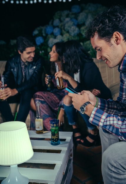 Retrato de homem feliz olhando seu smartphone em uma festa ao ar livre com amigos. conceito de amizade e celebrações.