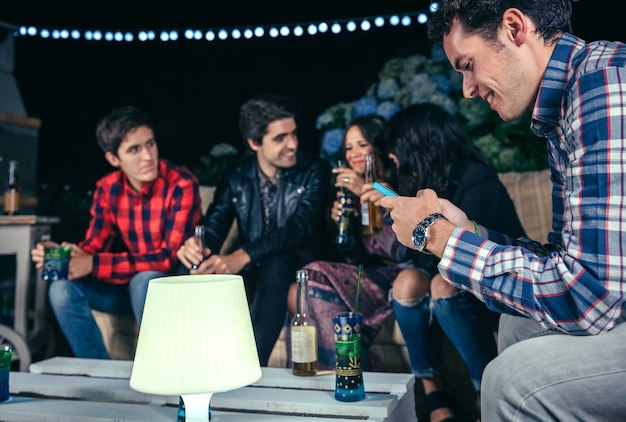 Retrato de homem feliz olhando seu smartphone em uma festa ao ar livre com amigos. conceito de amizade e celebrações.
