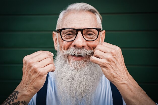 Foto retrato de homem feliz sênior hippie com parede verde - foco no bigode