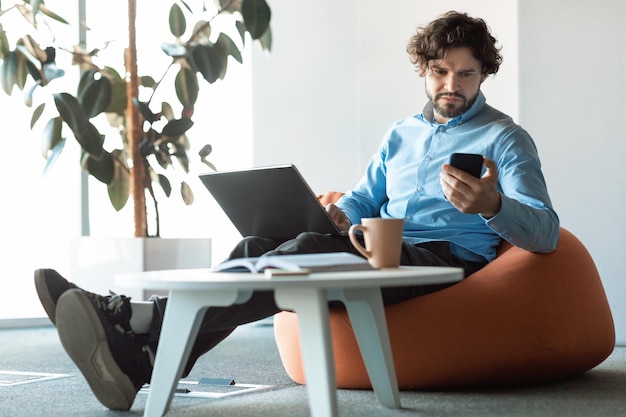 Foto retrato de homem focado usando smartphone e pc no escritório