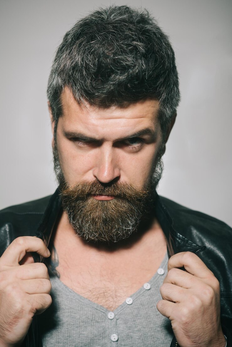 Foto retrato de homem. homem barbudo elegante de pulôver cinza e jaqueta de couro preta da moda. homem caucasiano sério com barba e bigode mantém a gola da jaqueta. retrato de closeup atraente homem barbudo sexy
