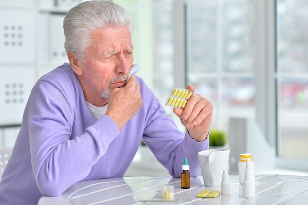 Retrato de homem idoso doente com pílulas posando em casa