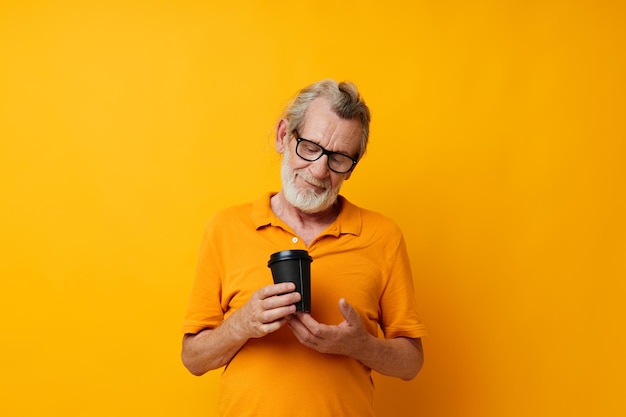 Retrato de homem idoso em uma camiseta amarela um copo com uma bebida de fundo amarelo