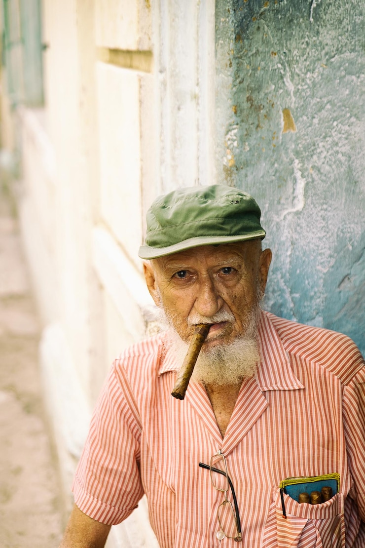 Foto retrato de homem idoso vestindo boné fumando charuto enquanto está sentado ao ar livre