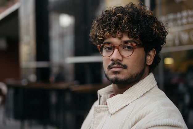 Foto retrato de homem indiano pensativo usando óculos olhando para a câmera na rua, copie o espaço