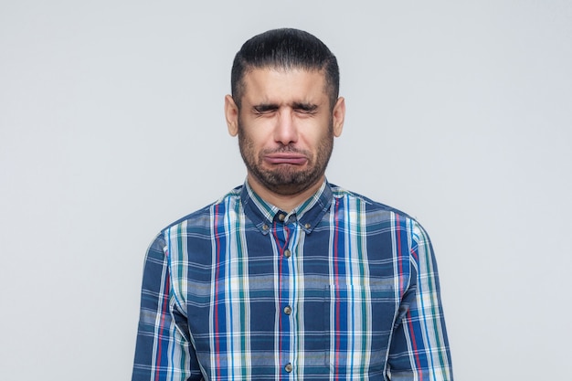 Retrato de homem infeliz e deprimido com cabelo preto, sentindo-se envergonhado ou doente, mantendo os olhos fechados. Conceito de expressões e emoções do rosto humano. Estúdio isolado em fundo cinza.