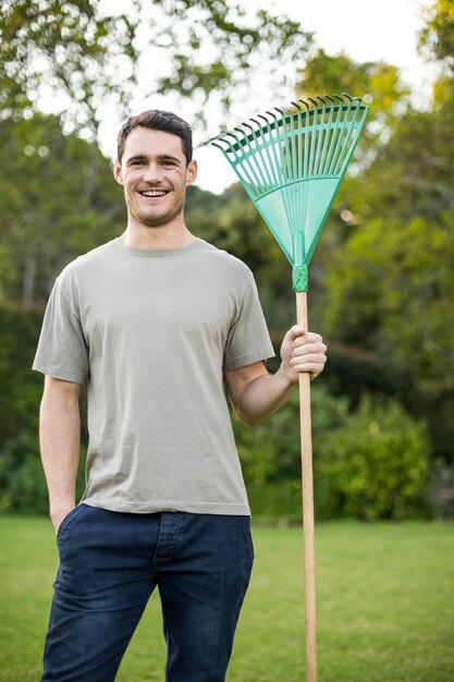 Retrato, de, homem jovem, ficar, com, um, ancinho ajardinando, em, jardim