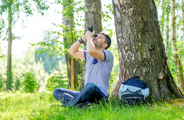 Retrato de homem jovem hippie com câmera ao ar livre. Jovem fotógrafo masculino fotografando a natureza num dia de verão.
