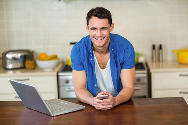 Retrato, de, homem jovem, inclinar-se, worktop cozinha, com, móvel, e, laptop