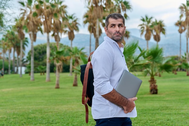 Retrato de homem maduro confiante sério com laptop ao ar livre