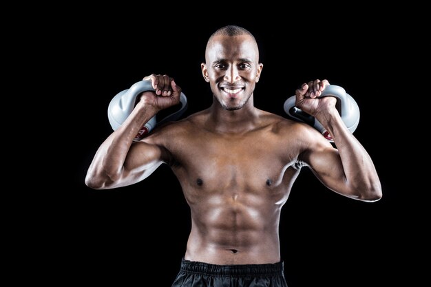 Retrato de homem muscular feliz exercitando com kettlebells