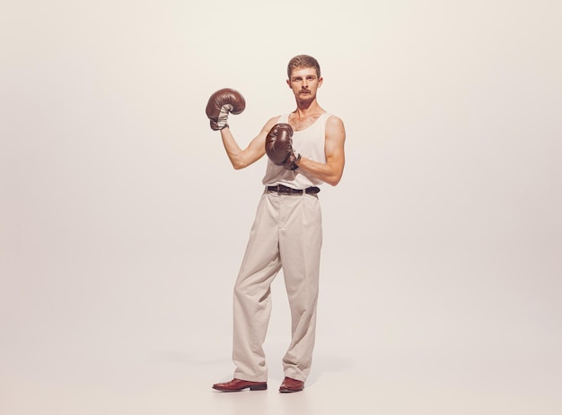 Retrato de homem musculoso em roupas vintage mostrando músculos em luvas de boxe posando isolado sobre