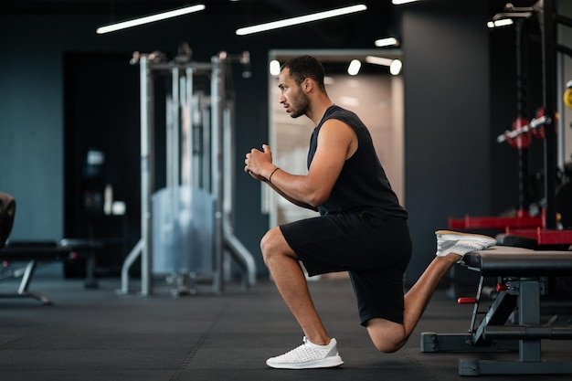 Retrato de homem negro atlético fazendo exercício de agachamento búlgaro no ginásio