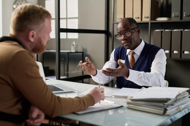 Retrato de homem negro sênior como cliente de consultoria de advogado no escritório e gesticulando