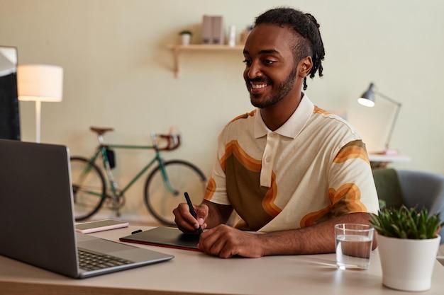 Retrato de homem negro sorridente como artista digital ou fotógrafo usando caneta tablet no local de trabalho