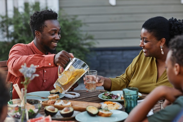 Retrato de homem negro sorridente derramando limonada em vidro durante o jantar em família ao ar livre