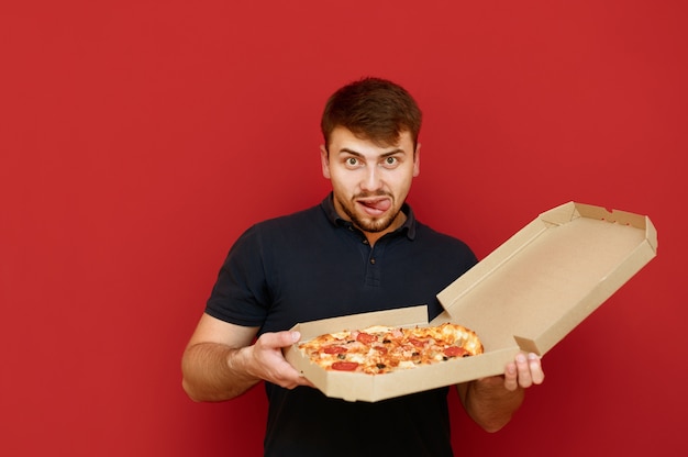 Retrato de homem positivo se levanta e abre uma caixa de deliciosa pizza fresca
