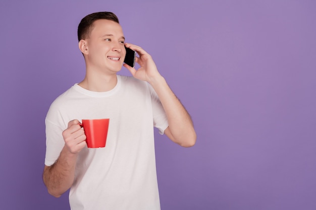 Retrato de homem positivo segurar conversa ao telefone olhar espaço vazio beber chá no fundo roxo