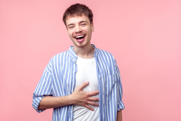 Retrato de homem ruivo feliz engraçado com barba pequena e bigode em camisa listrada casual segurando sua barriga e rindo alto, ouvindo piada. tiro de estúdio interior isolado no fundo rosa