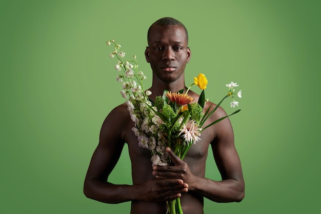 Retrato de homem sem camisa africano segurando lindo buquê olhando para câmera isolada em fundo verde