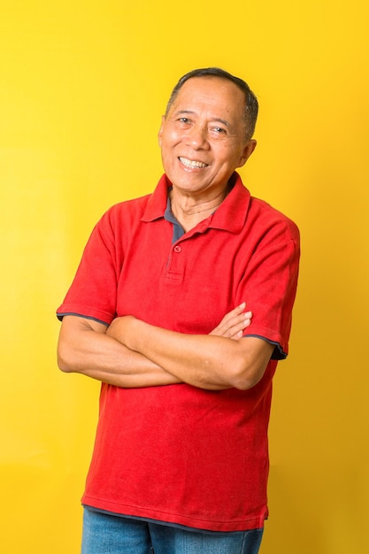 Retrato de homem sênior asiático usa camiseta vermelha com braços cruzados isolados em fundo amarelo